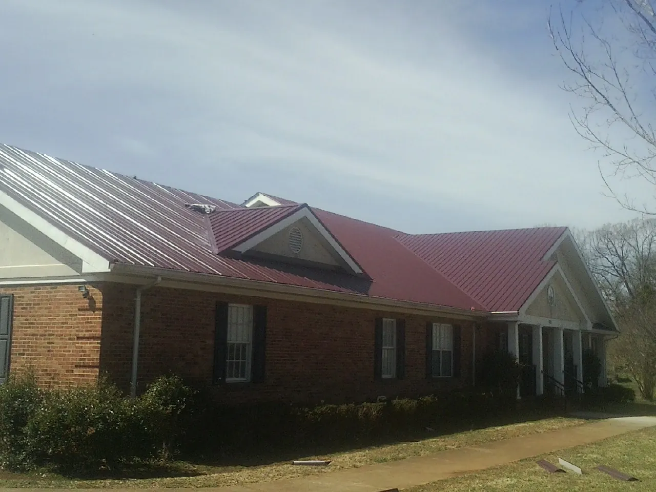 Red metal roof with gabled entries on a long brick building, from a Hail Damage Roof Repair job in Bryans Road
