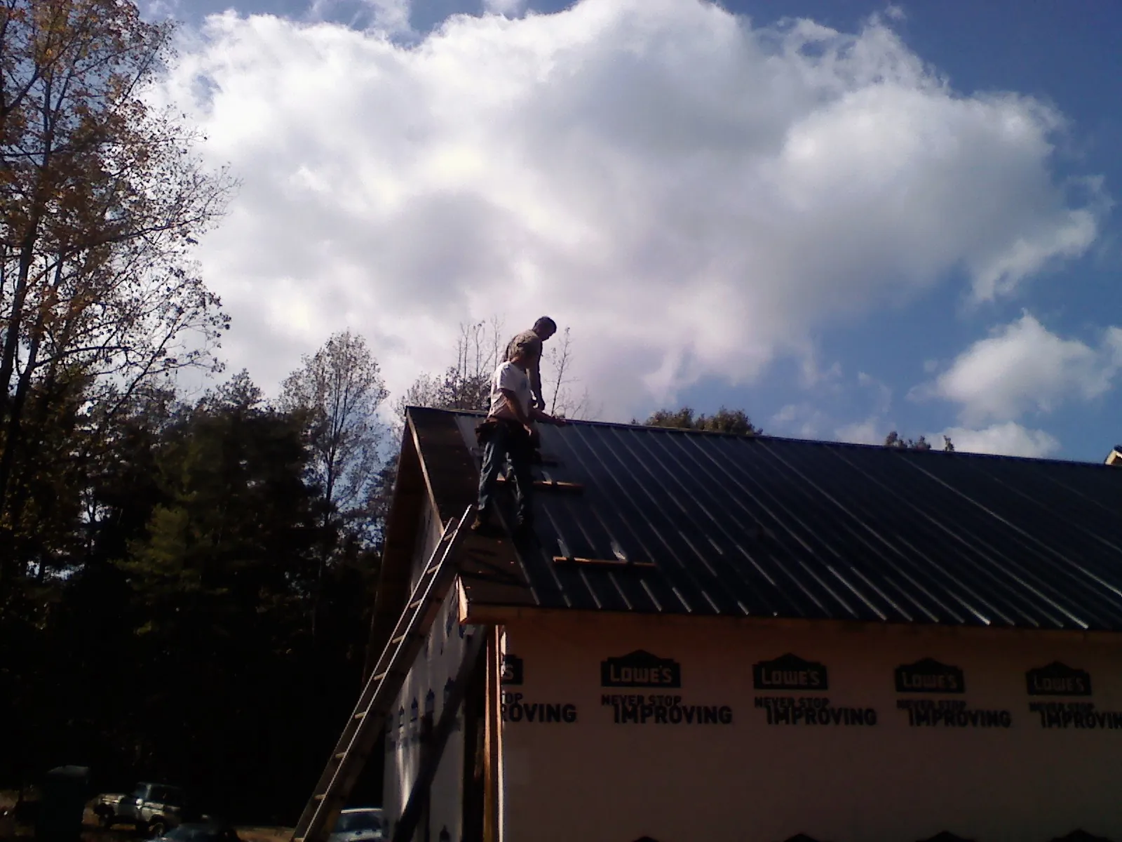 Roofer fastening dark metal panels high against a cloudy sky, from a Roof Inspection job in Bryans Road