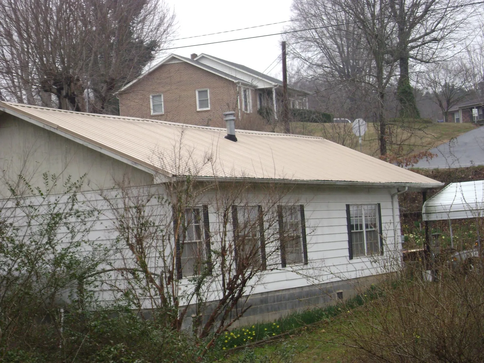 Tan metal roof on a white sided house set into a hillside — Commercial Roofing by Roofing Brothers in Bryans Road